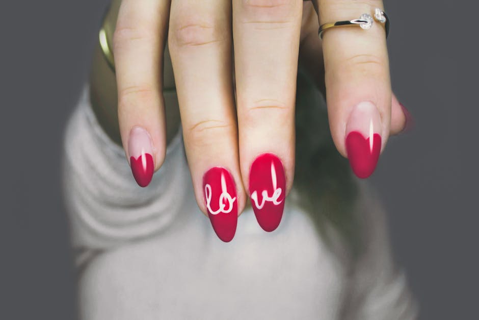 Vibrant red nails with 'love' art on a woman's hand, showcasing elegant style and design